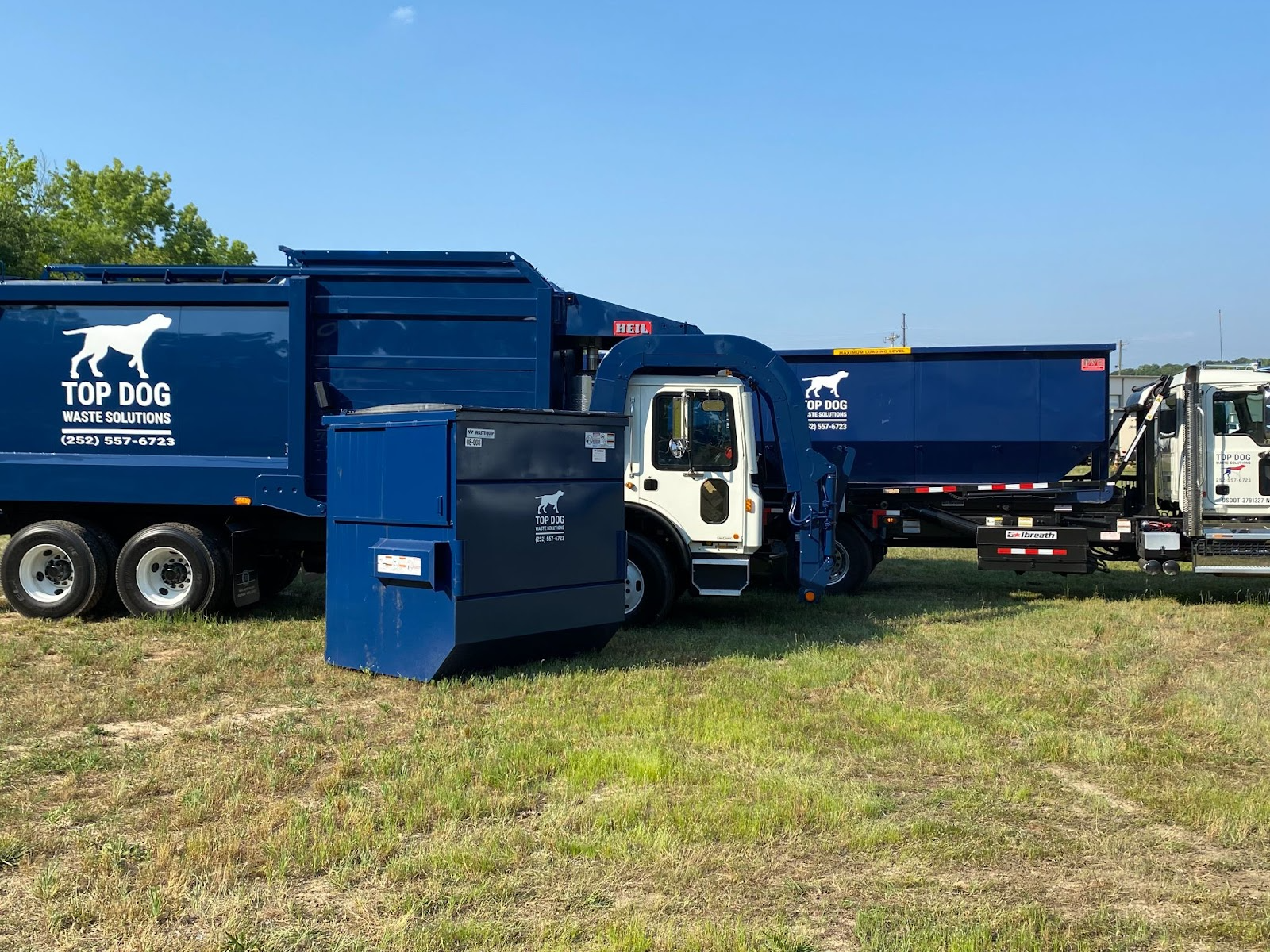 Top Dog Waste Solutions hauling truck with a roll-off dumpster loaded and a front-load dumpster placed on the ground in front. 