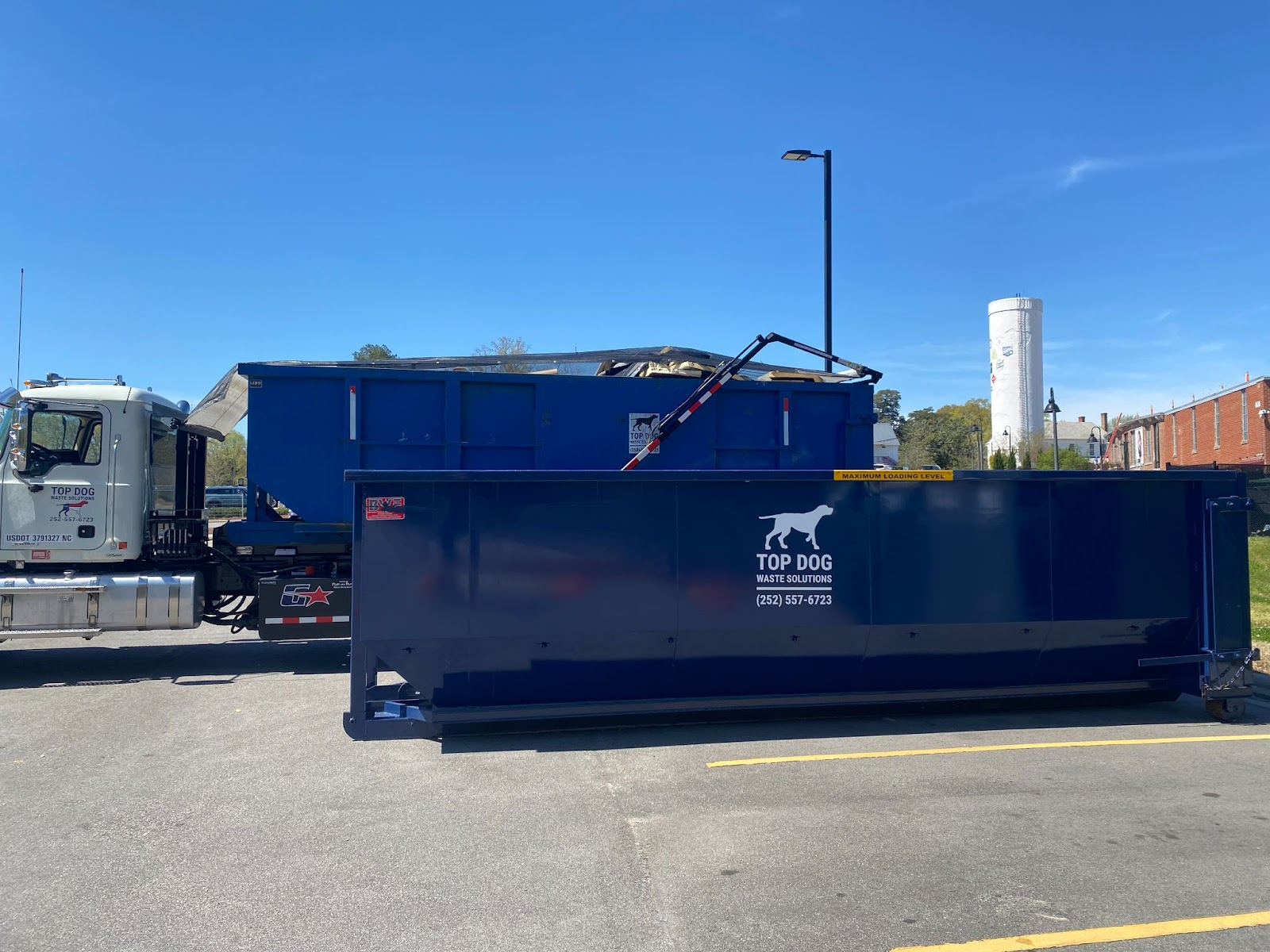 Top Dog Waste Solutions truck with one blue industrial dumpster loaded and another on the ground, ready for site delivery.