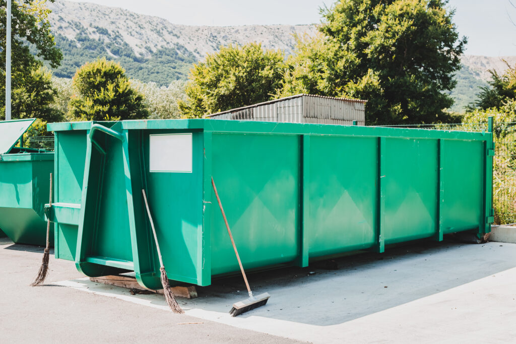 A dumpster surrounded by brooms on a jobsite.