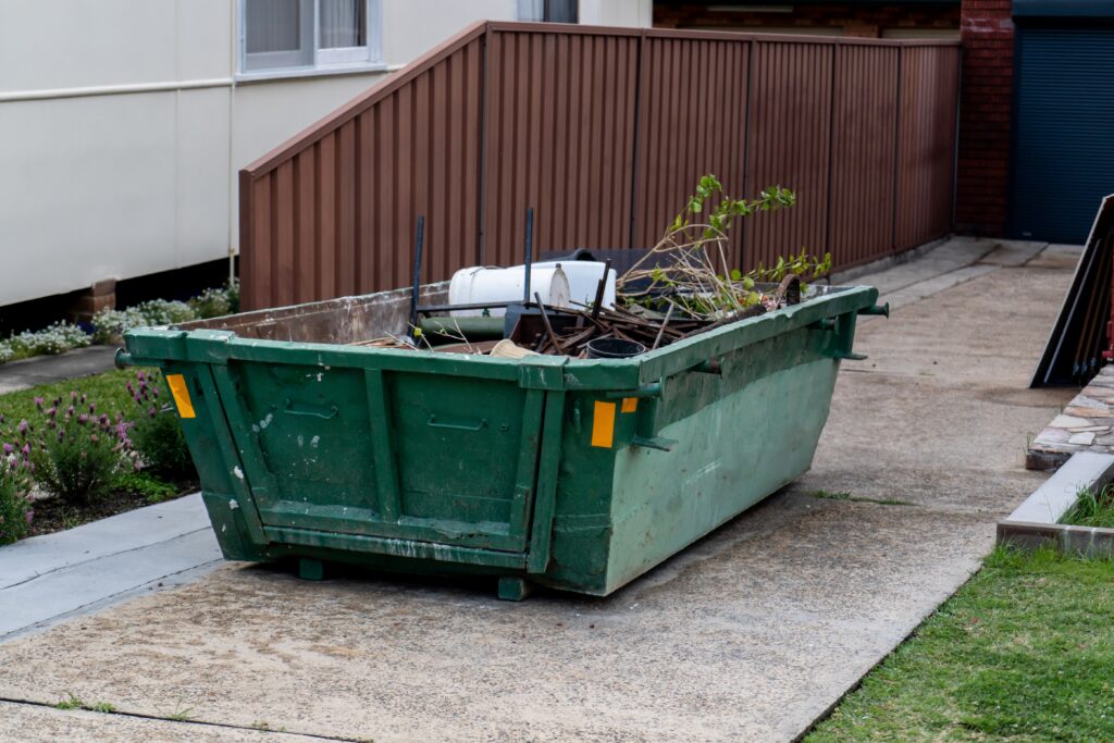 Mix of green waste and general trash loaded into a short dumpster in a driveway.