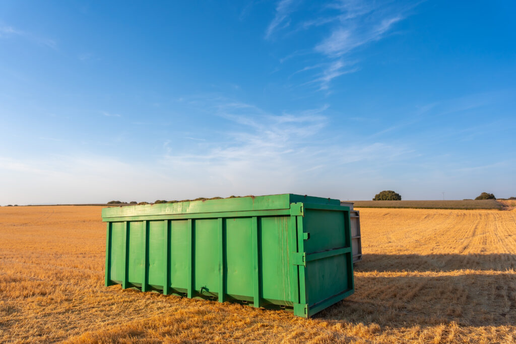 A large green dumpster sits in an open field.