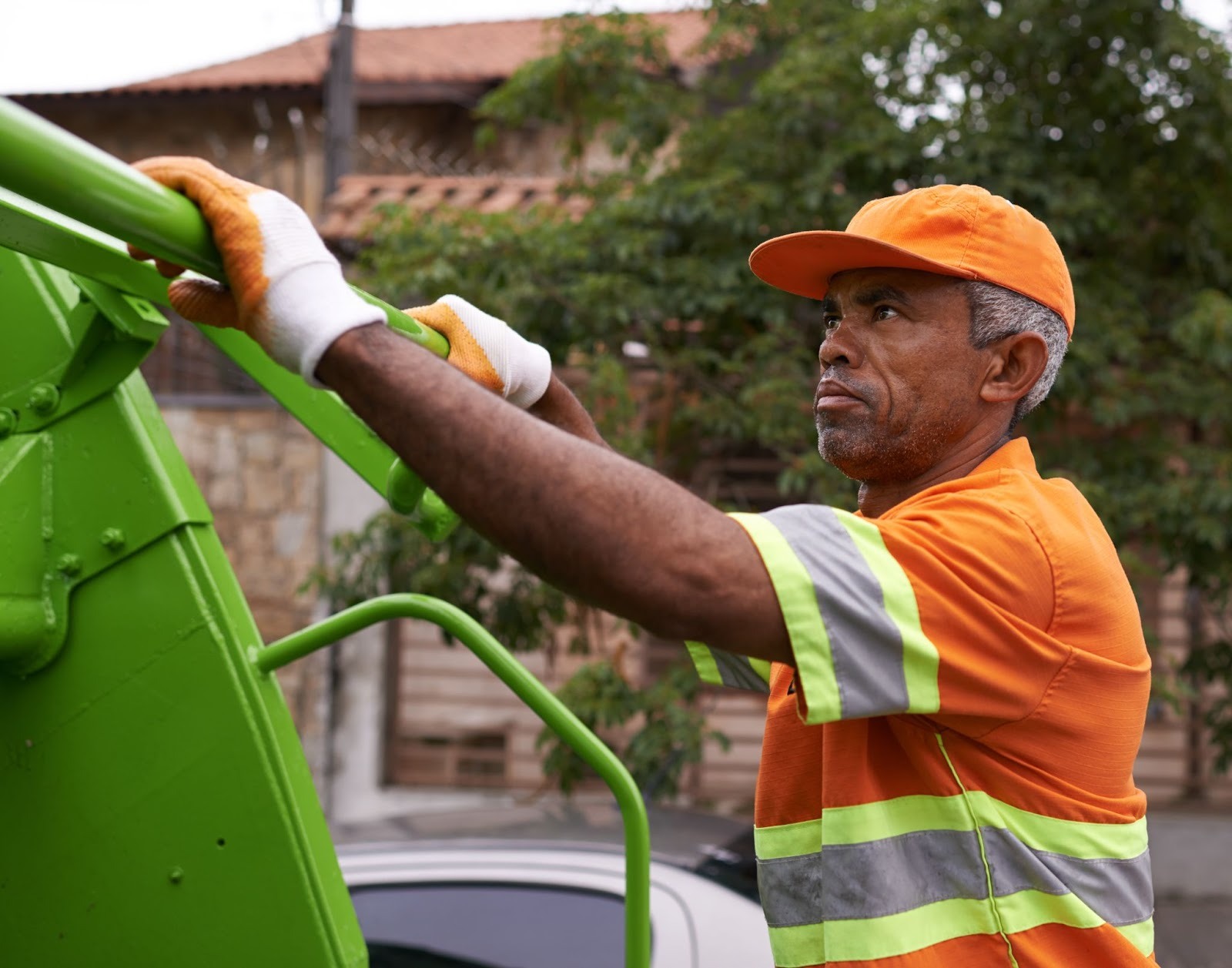 Closeup on a trash collector riding on the back of his truck.