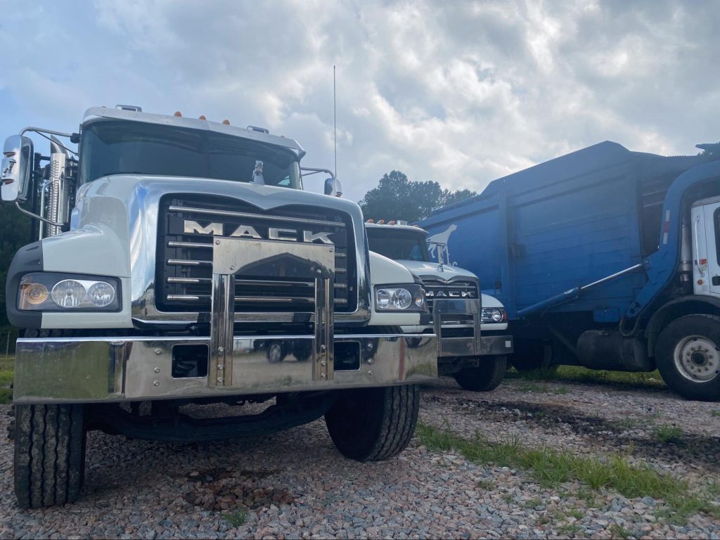 Three junk hauling trucks on gravel. 