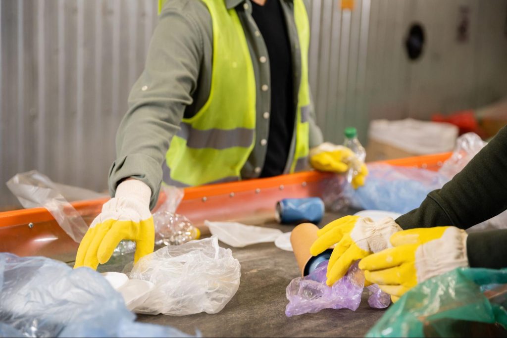 Workers in safety vests and gloves sorting waste at a recycling center.